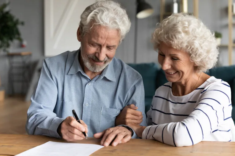 60s elderly spouses at lawyer office sitting at desk hoary husband holding pen family ready sign marriage contract make legal formalities at notary, bequeath savings and property to children concept